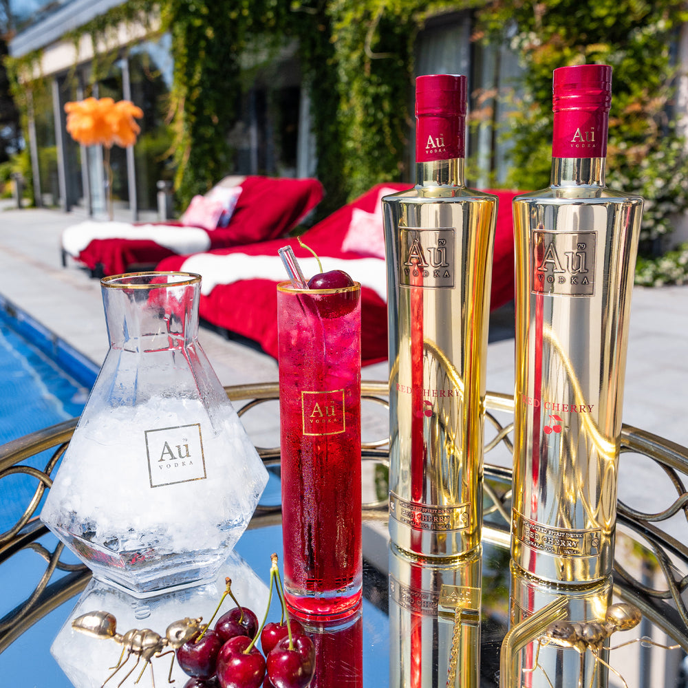Au Vodka Red Cherry bottle and glassware bundle with ice and cherries on a mirrored tray by a pool